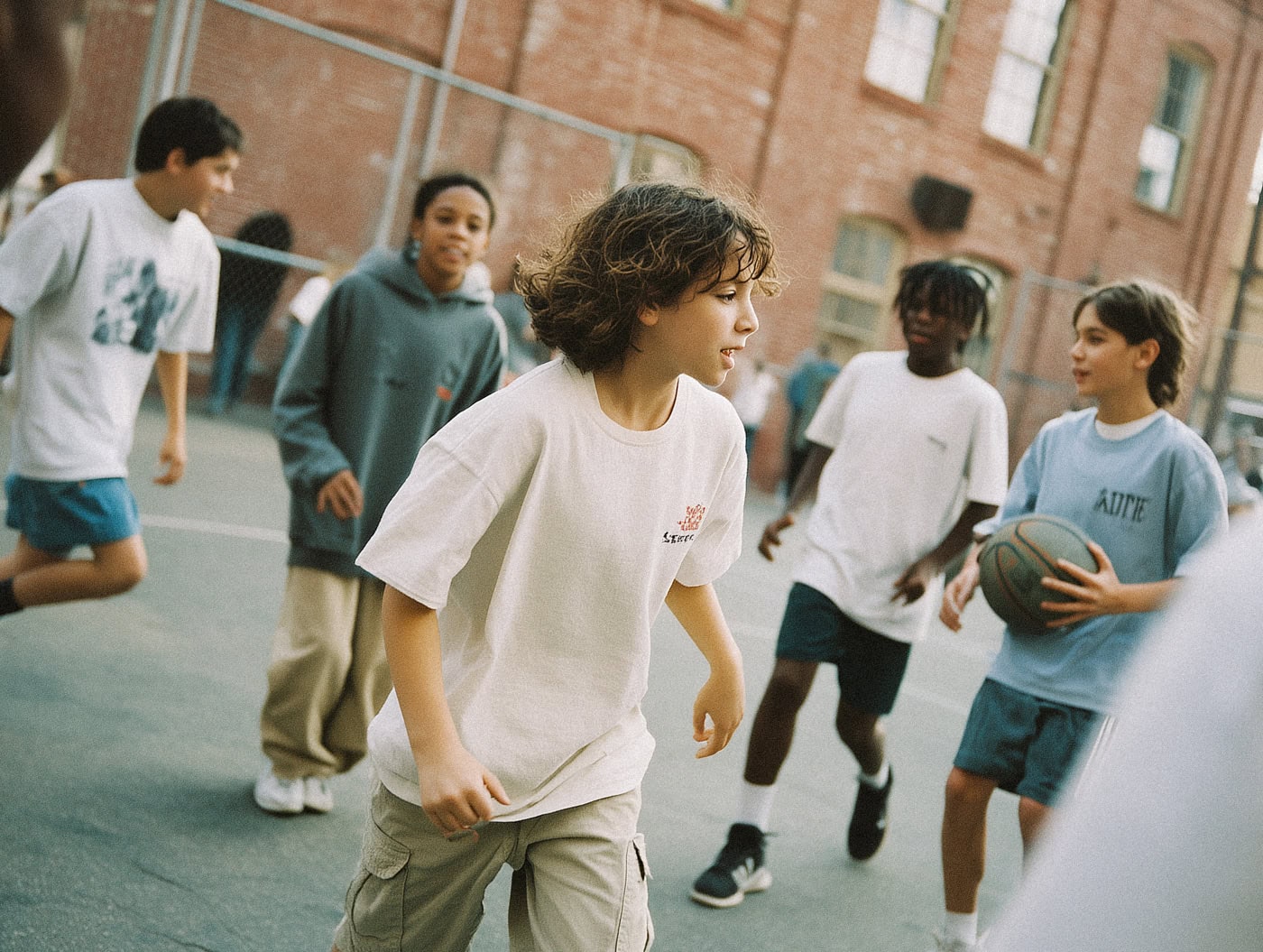 Mehrere Jugendliche bewegen sich über einen Basketballplatz, einer hält den Ball.